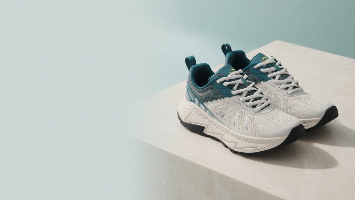 A pair of white Slazenger Warren sneakers with teal panels on a stone plinth